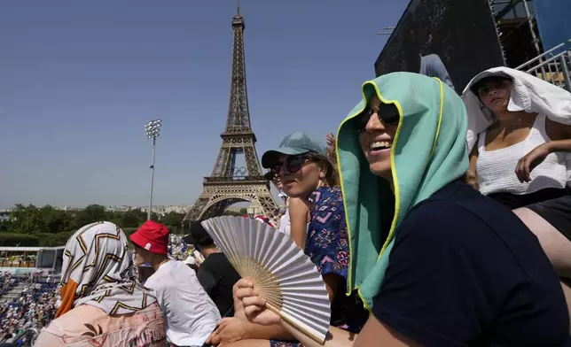 FILE - Stephanie Touissaint, foreground, uses a fan to keep cool in the sweltering heat at Eiffel Tower Stadium during a beach volleyball match between Cuba and Brazil at the 2024 Summer Olympics, July 30, 2024, in Paris, France. (AP Photo/Robert F. Bukaty, File)