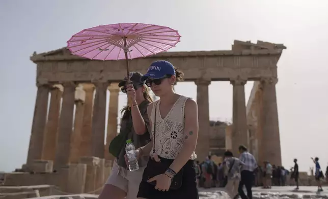 FILE - Tourists with an umbrella walk in front of the Parthenon at the ancient Acropolis in central Athens, June 12, 2024. (AP Photo/Petros Giannakouris, File)