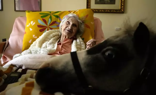 Elli Salma, a resident of an elderly care home, looks up as Ivi, a miniature horse used for therapy programs, visits her room, in Athens, Greece, on Friday, Nov. 22, 2024. (AP Photo/Thanassis Stavrakis)