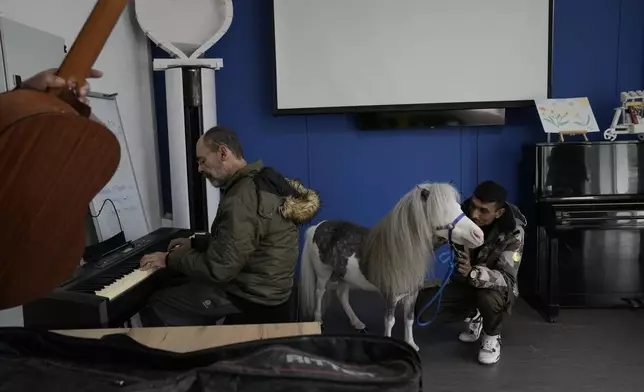 Haris, a resident of a psychiatric clinic for adults, left, plays a farewell song in piano for Homer, a miniature horse used for therapy programs, in Nea Makri, about 38 kilometres (60m miles) east of Athens, Greece, on Friday, Nov. 15, 2024. (AP Photo/Thanassis Stavrakis)