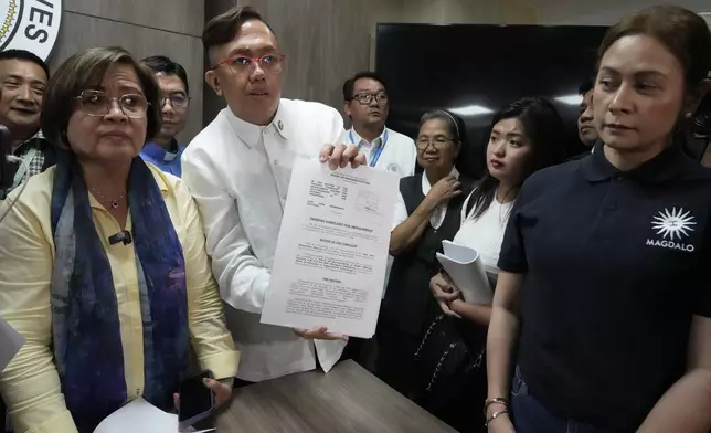 Akbayan Partylist representative Perci Cendana, center, shows a received copy of an impeachment complaint they filed Monday Dec. 2, 2024 against Philippine Vice President Sara Duterte by several prominent opponents and activists, including former Senator Leila de Lima, left, at the House of Representatives in Quezon City, Philippines. (AP Photo/Aaron Favila)