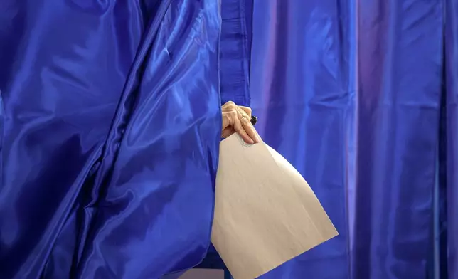 A woman holding a ballot exits a voting booth during the country's parliamentary elections, in Bucharest, Romania, Sunday, Dec. 1, 2024. (AP Photo/Andreea Alexandru)