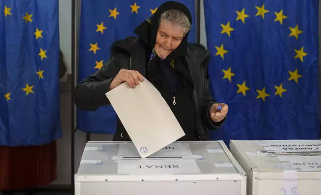 A woman casts her vote in a station with European Union flags as curtains for the cabins, in the country's parliamentary elections, in Baleni, Romania, Sunday, Dec. 1, 2024. (AP Photo/Vadim Ghirda)