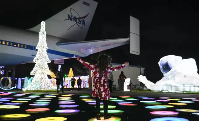 A child plays among space-themed holiday lights near a replica of shuttle Independence at Space Center Houston on Monday, Dec. 9, 2024, in Houston. (AP Photo/Ashley Landis)