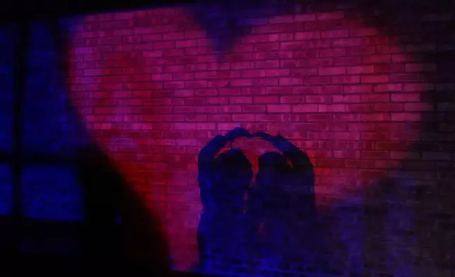 Visitors are silhouetted as they make heart sign while they walk through "Courtyard of Love" as part of the Chicago Botanic Garden's 1.3-mile, sixth annual Lightscape holiday experience of light and music in Glencoe, Ill., Wednesday, Dec. 4, 2024. (AP Photo/Nam Y. Huh)