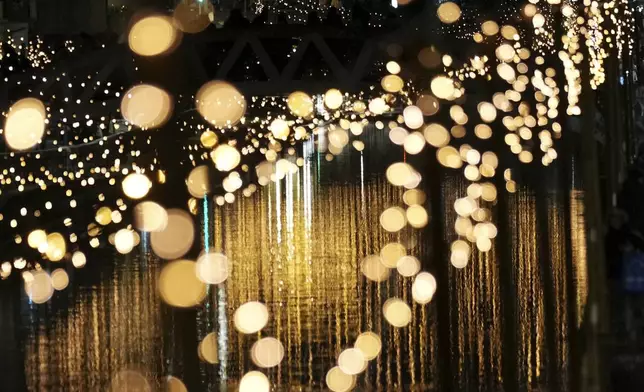 People stand on a bridge as Christmas lights illuminate the Darsena dei Navigli, the neighborhood named for the canals that run through this area of Milan, Italy, Monday, Dec. 9, 2024. (AP Photo/Antonio Calanni)