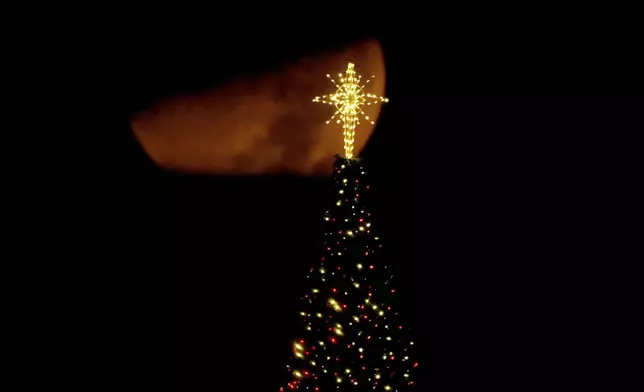 The moon sets beyond a Christmas tree on top of an office building, Monday, Dec. 9, 2024, in Overland Park, Kan. (AP Photo/Charlie Riedel)