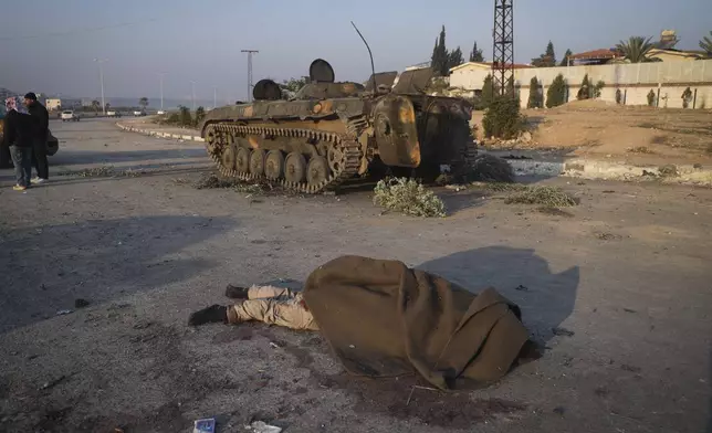 The body of a government soldier lies next to a armoured vehicle in a street in Hama, Syria, Friday Dec. 6, 2024.(AP Photo/Omar Albam)