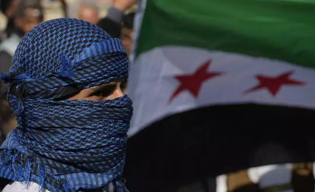 A Syrian man stands in front of a flag during a spontaneous demonstration celebrating the fall of the Assad regime in Nicosia, Cyprus, Sunday, Dec. 8, 2024. (AP Photo/Petros Karadjias)