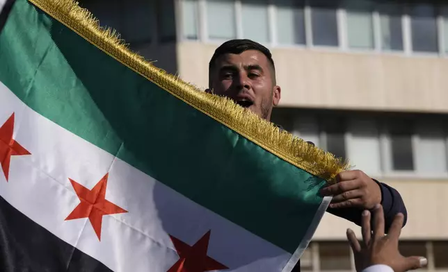 A Syrian man waves a flag during a spontaneous demonstration celebrating the fall of the Assad regime, in Nicosia, Cyprus, Sunday, Dec. 8, 2024. (AP Photo/Petros Karadjias)