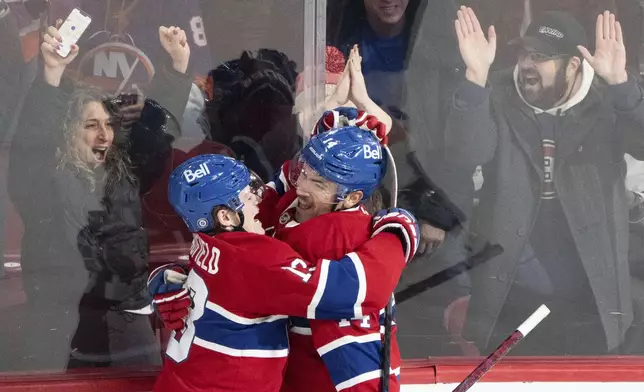 Montreal Canadiens' Nick Suzuki (14) celebrates his game-winning goal against the New York Islanders with teammate Cole Caufield (13) during overtime in an NHL hockey game in Montreal, Tuesday, Dec. 3, 2024. (Christinne Muschi/The Canadian Press via AP)