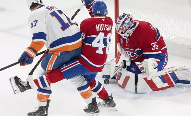 Montreal Canadiens goaltender Sam Montembeault (35) stops a shot by New York Islanders' Matt Martin (17) as Canadiens' Lane Hutson (48) defends during the third period of an NHL hockey game in Montreal, Tuesday, Dec. 3, 2024. (Christinne Muschi/The Canadian Press via AP)