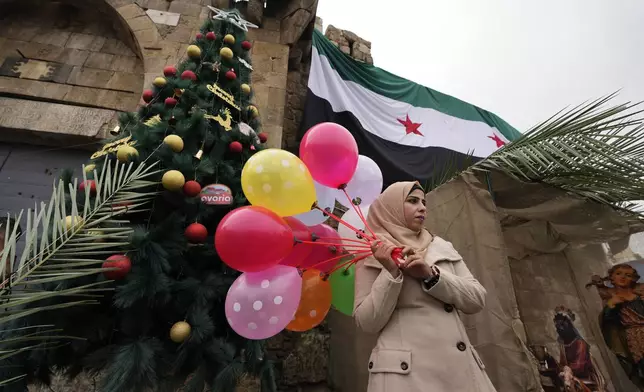 A Syrian Muslim woman poses for a picture in front of a Christmas tree in Bab Touma neighbourhood, in Damascus, Syria, Tuesday, Dec. 24, 2024. (AP Photo/Hussein Malla)