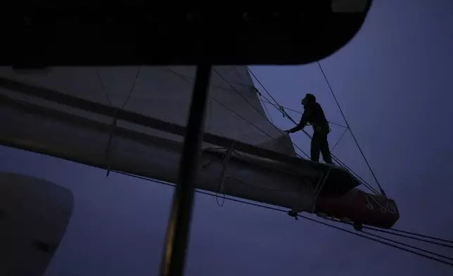 A sailor stands on the boom to check the folding of the mainsail of the sailboat ''Grain de Sail II' as it sails off Saint Malo, western France, Nov. 6, 2024. (AP Photo/Thibault Camus)