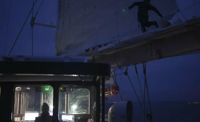 A sailor stands on the boom to check the folding of the mainsail of the sailboat 'Grain de Sail II' as it sails off Saint Malo, western France, Nov. 6, 2024. (AP Photo/Thibault Camus)