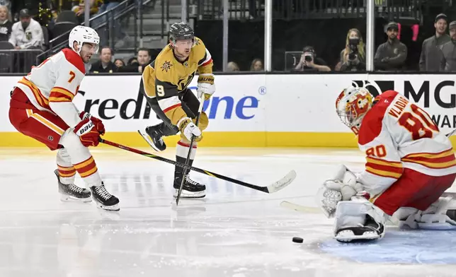 Vegas Golden Knights center Jack Eichel (9) shoots against Calgary Flames defenseman Kevin Bahl (7) and goaltender Dan Vladar (80) during the second period of an NHL hockey game Sunday, Dec. 29, 2024, in Las Vegas. (AP Photo/David Becker)