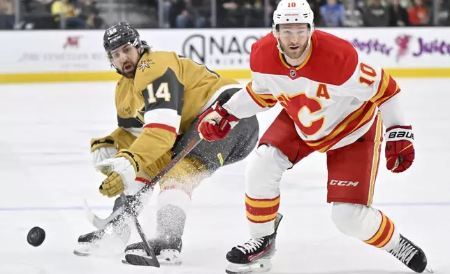 Vegas Golden Knights defenseman Nicolas Hague (14) and Calgary Flames center Jonathan Huberdeau (10) vie for the puck during the second period of an NHL hockey game Sunday, Dec. 29, 2024, in Las Vegas. (AP Photo/David Becker)