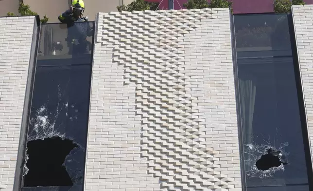 A firefighter checks the broken widows at a hotel in Bangkok, Thailand, Monday, Dec. 30, 2024 after a fire. (AP Photo/Sakchai Lalit)