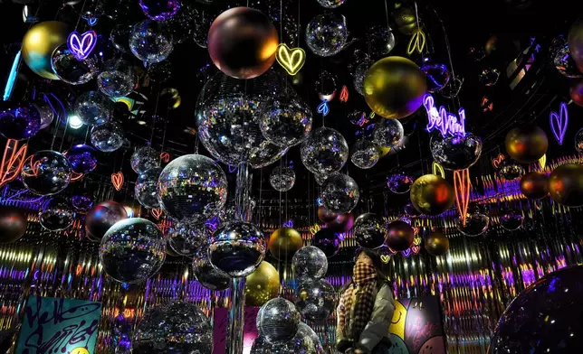 A woman looks at the disco and Christmas balls illuminated with lights hanging on a decoration display for the upcoming Christmas Festival at a popular outdoor shopping mall in Beijing, Wednesday, Dec. 18, 2024. (AP Photo/Andy Wong)