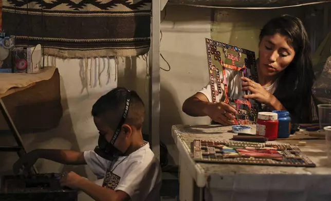 Dana Lopez, right, paints a board for poleana, a board game invented in prison, while her son Kevin plays in their workshop in the State of Mexico, Mexico, Friday, Oct. 25, 2024. (AP Photo/Ginnette Riquelme)