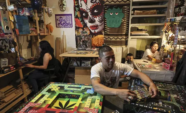 Diego Gonzalez, center, holds a pack of tokens for poleana, a board game invented in prison, alongside designer Carolina Duran, left, and Dana Lopez, his partner, with their son Kevin in the State of Mexico, Mexico, Friday, Oct. 25, 2024. (AP Photo/Ginnette Riquelme)