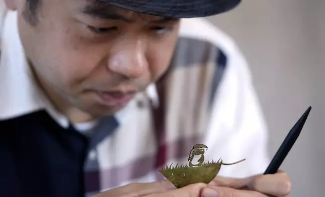 Japanese leaf-cutting artist, who goes by the name Lito, looks at his work featuring a frog with an umbrella, during an interview in Tokyo Wednesday, Nov. 27, 2024. (AP Photo/Shuji Kajiyama)