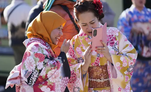 A woman from Nagoya, left, and her friend from Tokyo, both originally from Indonesia, react to their photos they just took as they visit Sensoji Buddhist temple on New Year's Eve in Tokyo, Tuesday, Dec. 31, 2024. (AP Photo/Hiro Komae)