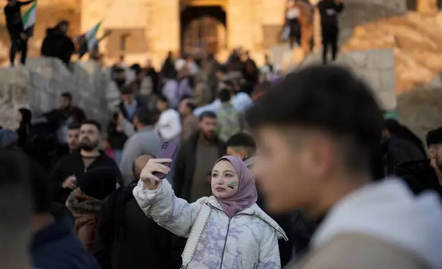 A Syrian girl with the colours of the "revolutionary" Syrian flag on her face, takes a selfie in front of the ancient Aleppo Citadel in the old city of Aleppo, Syria, Saturday, Dec. 14, 2024. (AP Photo/Khalil Hamra)