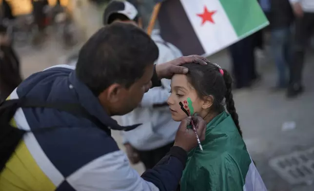 A man draws the "revolutionary" Syrian flag on a girl's face at the ancient Aleppo Citadel in the old city of Aleppo, Syria, Saturday, Dec. 14, 2024. (AP Photo/Khalil Hamra)