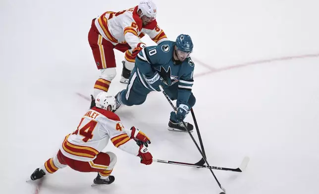 San Jose Sharks center Klim Kostin (10) controls the puck against Calgary Flames defenseman Joel Hanley (44) and defenseman MacKenzie Weegar (52) during the third period of an NHL hockey game Saturday, Dec. 28, 2024, in San Jose, Calif. (AP Photo/Eakin Howard)