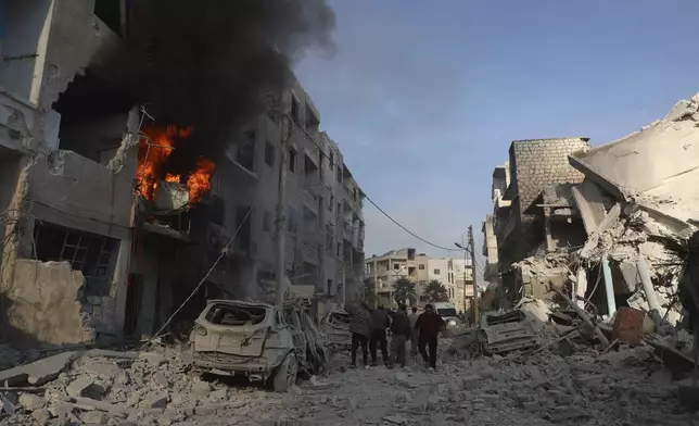 This photo provided by the Syrian Civil Defence White Helmets, which has been authenticated based on its contents and other AP reporting, shows Syrian residents gather near destroyed buildings, after Syrian government forces hit Idlib city, Syria, Monday, Dec. 2, 2024. (Syrian Civil Defence White Helmets via AP)