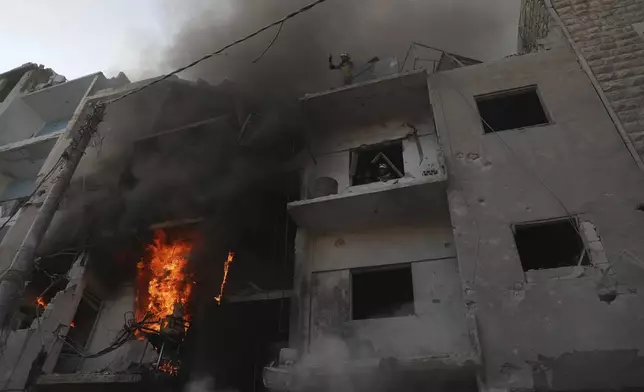 This photo provided by the Syrian Civil Defence White Helmets, which has been authenticated based on its contents and other AP reporting, shows Syrian White Helmet civil defence workers stand in a burning building after the Syrian government forces hit Idlib city, Syria, Monday, Dec. 2, 2024. (Syrian Civil Defence White Helmets via AP)