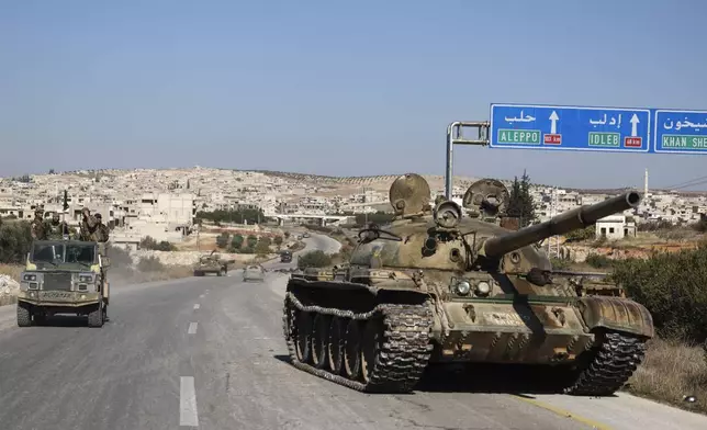 Syrian opposition fighters drive by an abandoned Syrian army armoured vehicle on a highway in the outskirts of in Khan Sheikhoun, southwest of Aleppo, Sunday, Dec. 1, 2024. Syrian opposition insurgency launched a campaign on Wednesday with a two-pronged attack on Aleppo and the countryside around Idlib.(AP Photo/Ghaith Alsayed)