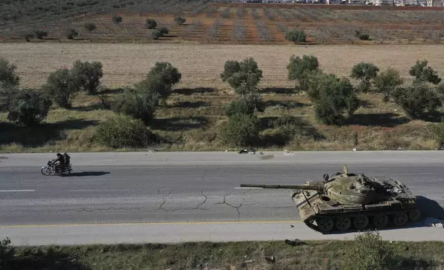 Syrian opposition fighters ride on a motorcycle by an abandoned Syrian army armoured vehicle on a road in the outskirts of in Khan Sheikhoun, southwest of Aleppo, Sunday, Dec. 1, 2024. Syrian opposition insurgency launched a campaign on Wednesday with a two-pronged attack on Aleppo and the countryside around Idlib.(AP Photo/Ghaith Alsayed)