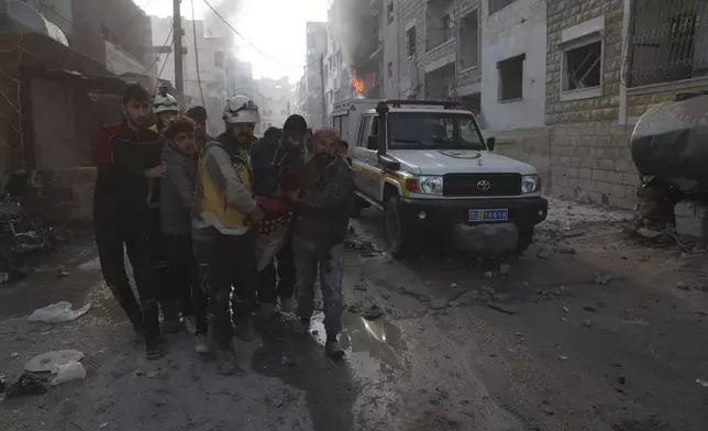 This photo provided by the Syrian Civil Defence White Helmets, which has been authenticated based on its contents and other AP reporting, shows a Syrian White Helmet civil defence worker and civilians carry a victim after the Syrian government forces hit Idlib city, Syria, Monday, Dec. 2, 2024. (Syrian Civil Defence White Helmets via AP)