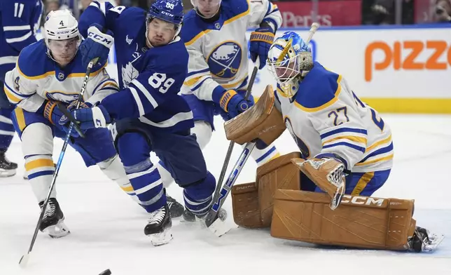 Toronto Maple Leafs left wing Nicholas Robertson (89) reaches for the puck in front of Buffalo Sabres goaltender Devon Levi, right, as Sabres' Bowen Byram (4) defends during second-period NHL hockey game action in Toronto, Sunday, Dec. 15, 2024. (Frank Gunn/The Canadian Press via AP)