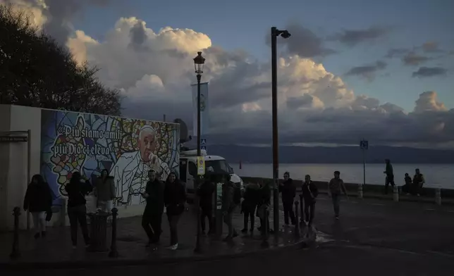 People walk past a mural featuring Pope Francis prior to the Pope's visit, in Ajaccio, in the southern French island of Corsica, Saturday, Dec. 14, 2024. (AP Photo/Thibault Camus)