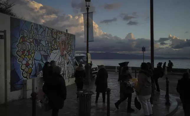 People walk past a mural featuring Pope Francis prior to the Pope's visit, in Ajaccio, in the southern French island of Corsica, Saturday, Dec. 14, 2024. (AP Photo/Thibault Camus)