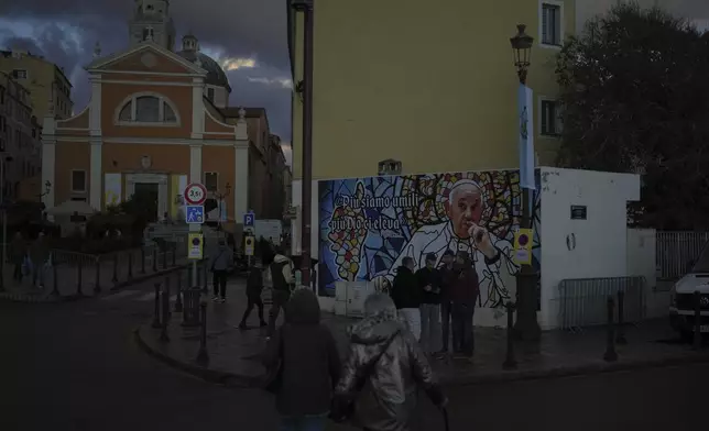 People walk past a mural featuring Pope Francis prior to the Pope's visit, in Ajaccio, in the southern French island of Corsica, Saturday, Dec. 14, 2024. (AP Photo/Thibault Camus)