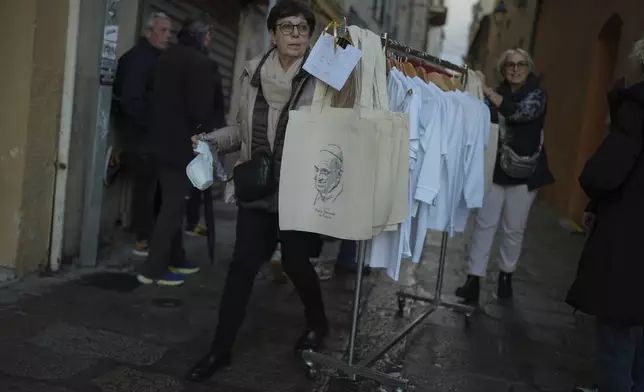 A woman carries bags bearing the Pope Franci' image prior to Pope's visit, in Ajaccio, in the southern French island of Corsica, Saturday, Dec. 14, 2024. (AP Photo/Thibault Camus)