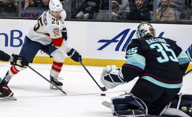 Florida Panthers forward Mackie Samoskevich (25), left, skates against Seattle Kraken goalie Joey Daccord during the first period of an NHL hockey game, Tuesday, Dec. 10, 2024, in Seattle. (AP Photo/Stephen Brashear)