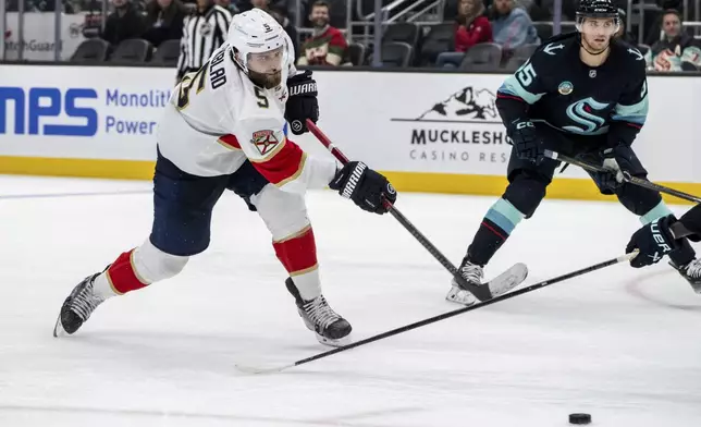 Florida Panthers defenseman Aaron Ekblad shoots the shoot the puck against Seattle Kraken forward Andre Burakovsky during the third period of an NHL hockey game, Tuesday, Dec. 10, 2024, in Seattle. The Panthers won 2-1 in a shootout. (AP Photo/Stephen Brashear)