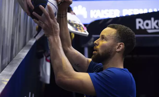 Golden State Warriors guard Stephen Curry gives autographs to fans before an NBA basketball game against the Dallas Mavericks, Sunday, Dec. 15, 2024, in San Francisco. (AP Photo/Benjamin Fanjoy)