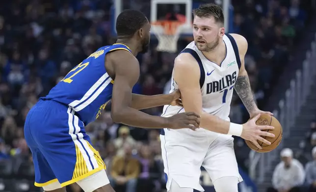 Golden State Warriors forward Andrew Wiggins, left, defends against Dallas Mavericks forward Luka Dončić, right, during the first half of an NBA basketball game Sunday, Dec. 15, 2024, in San Francisco. (AP Photo/Benjamin Fanjoy)