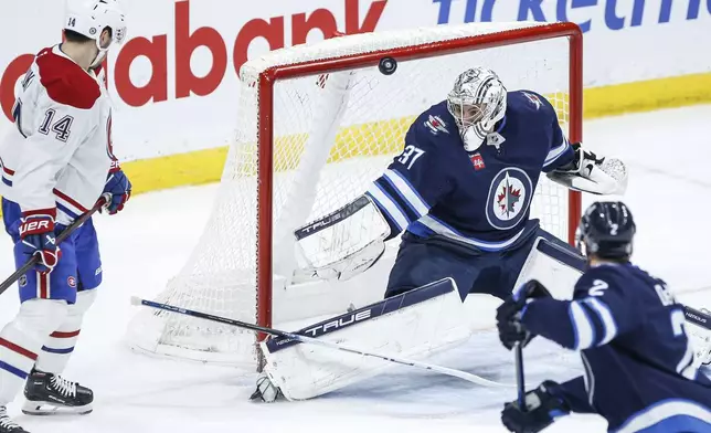 Winnipeg Jets goaltender Connor Hellebuyck (37) saves the shot as Montreal Canadiens' Nick Suzuki (14) waits for the rebound during the second period of an NHL hockey game, Saturday, Dec. 14, 2024 in Winnipeg, Manitoba. (John Woods/The Canadian Press via AP)