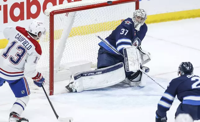 Winnipeg Jets goaltender Connor Hellebuyck (37) keeps his eyes on the puck as Montreal Canadiens' Cole Caufield (13) waits for the rebound during the second period of an NHL hockey game, Saturday, Dec. 14, 2024 in Winnipeg, Manitoba. (John Woods/The Canadian Press via AP)