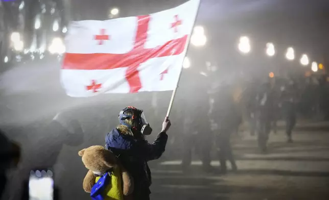 A demonstrator holds a Georgian national flag while being sprayed by a water cannon outside the parliament during a protest against the government's decision to suspend negotiations on joining the European Union in Tbilisi, Georgia, on Tuesday, Dec. 3, 2024. (AP Photo/Pavel Bednyakov)