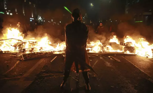 A demonstrator stands next to a burning barricade during a rally to protest against the government's decision suspending negotiations on joining the European Union in Tbilisi, Georgia, early Tuesday, Dec. 3, 2024. (AP Photo/Zurab Tsertsvadze)