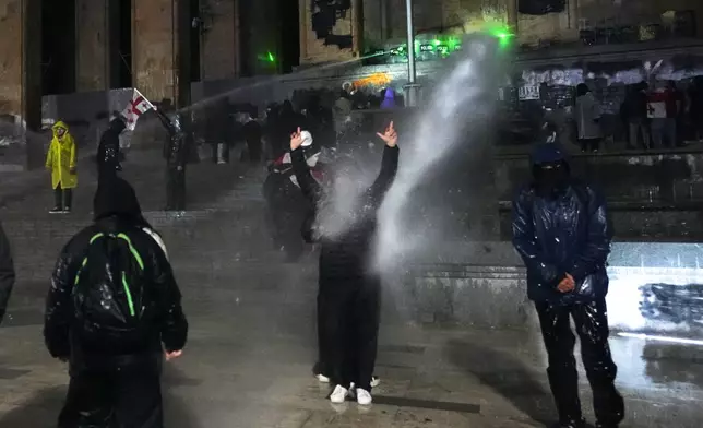 Demonstrators stand under running water from a water cannon rallying outside the parliament's building to continue protests against the government's decision to suspend negotiations on joining the European Union in Tbilisi, Georgia, Tuesday, Dec. 3, 2024. (AP Photo/Pavel Bednyakov)