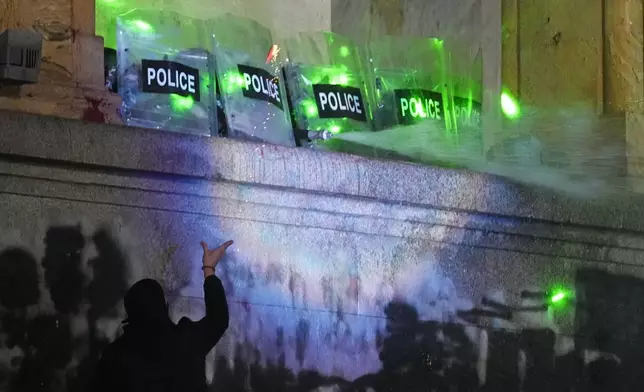 Demonstrators stand under running water from a fire-pump used by police rallying outside the parliament to continue protests against the government's decision to suspend negotiations on joining the European Union in Tbilisi, Georgia, on Tuesday, Dec. 3, 2024. (AP Photo/Pavel Bednyakov)